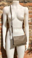 May include: A taupe leather crossbody bag with a flap closure and a long adjustable strap.