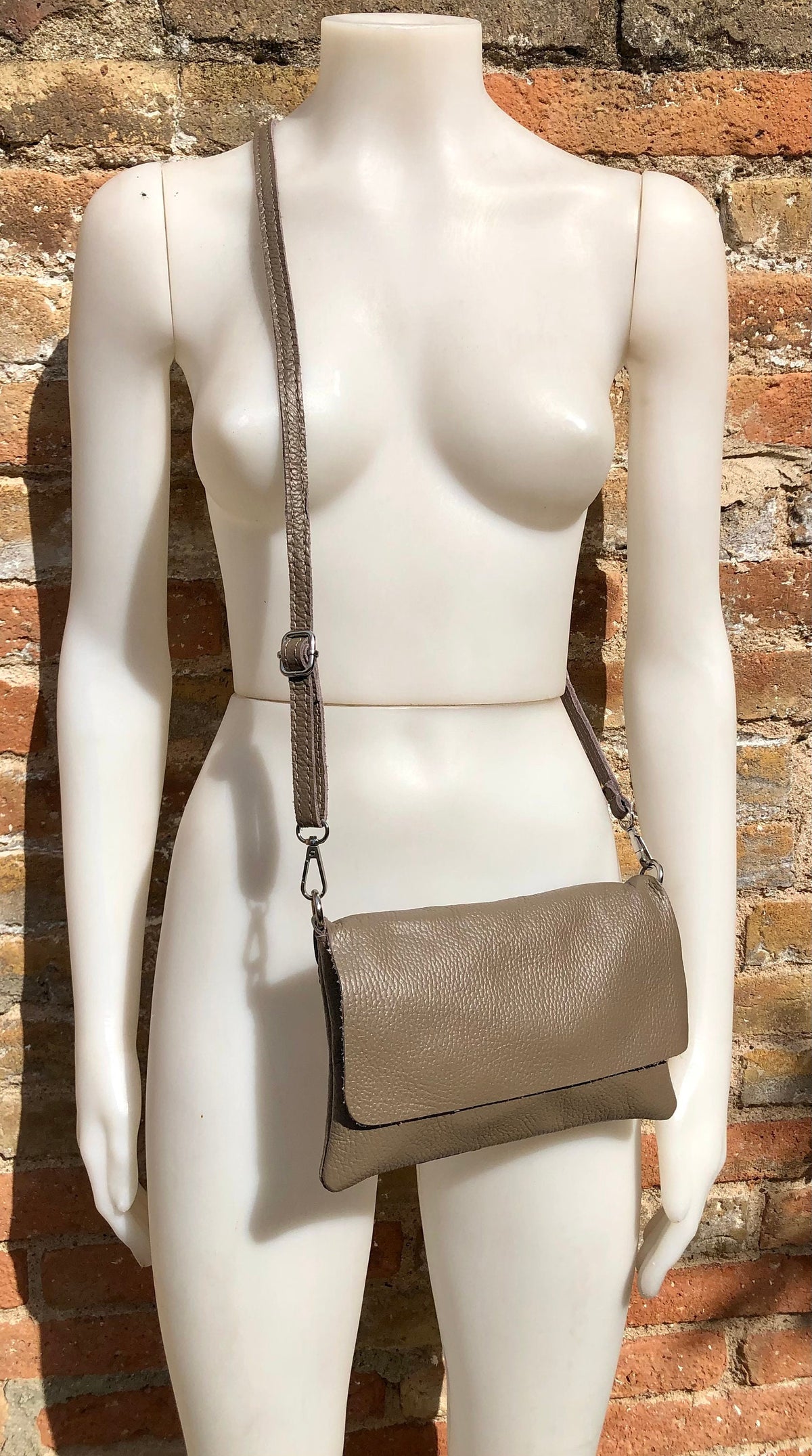 May include: A taupe leather crossbody bag with a flap closure and a long adjustable strap.