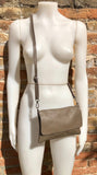 May include: A taupe leather crossbody bag with a flap closure and a long adjustable strap.