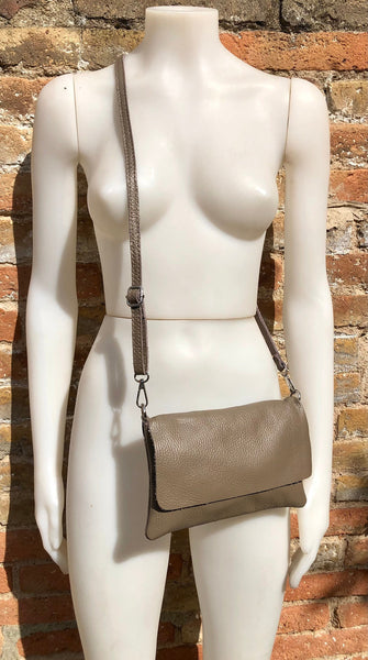 May include: A taupe leather crossbody bag with a flap closure and a long adjustable strap.