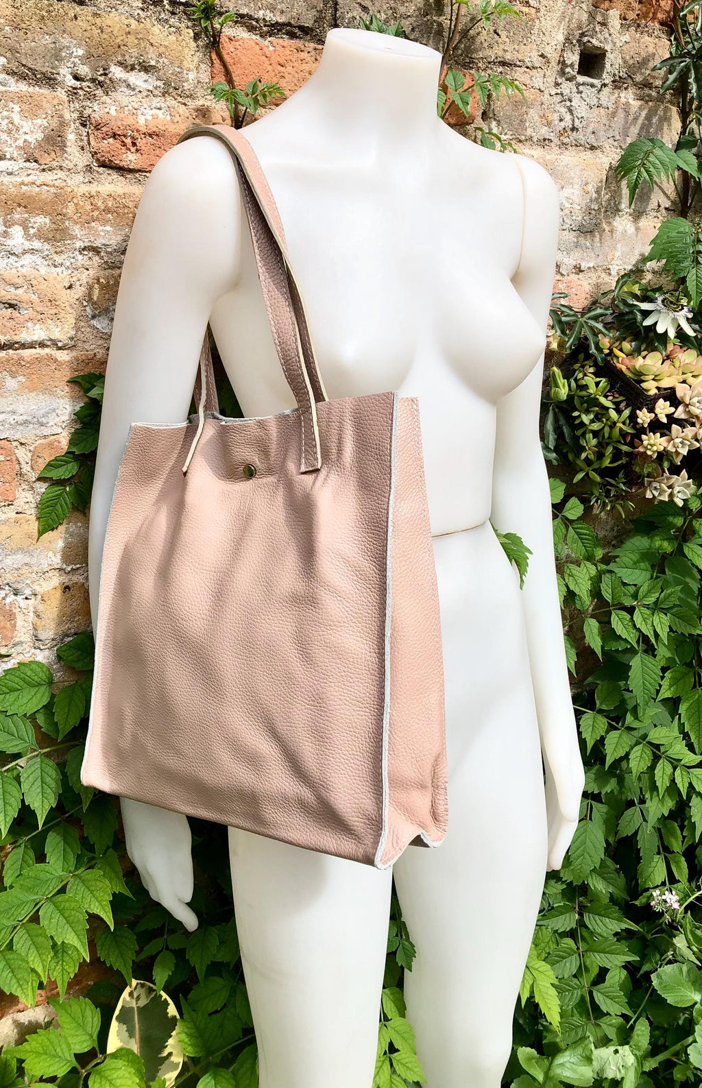 May include: A blush-pink leather tote bag with off-white contrast stitching. The bag features two shoulder straps and a subtle, minimalist design.  The leather appears soft and supple, with a slightly textured finish. The tote is roomy and spacious, ideal for everyday use. This stylish and functional bag is perfect for carrying essentials.