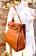 May include: A brown leather shoulder bag with a flap closure and a long strap. The bag is adorned with brass-colored studs along the edges and features a decorative stitched design on the flap. The bag is displayed on a white mannequin.