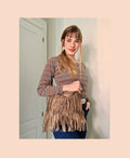 May include: A brown suede fringe bag with a long strap. The bag is worn by a person with long brown hair wearing a striped long-sleeved shirt and blue jeans.